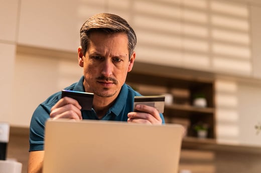 man holding two credit cards in front of a laptop