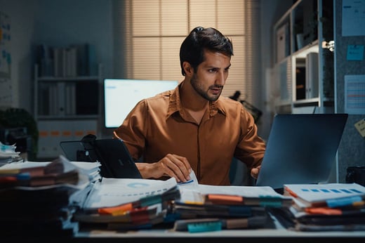 man with stacks of files and laptop