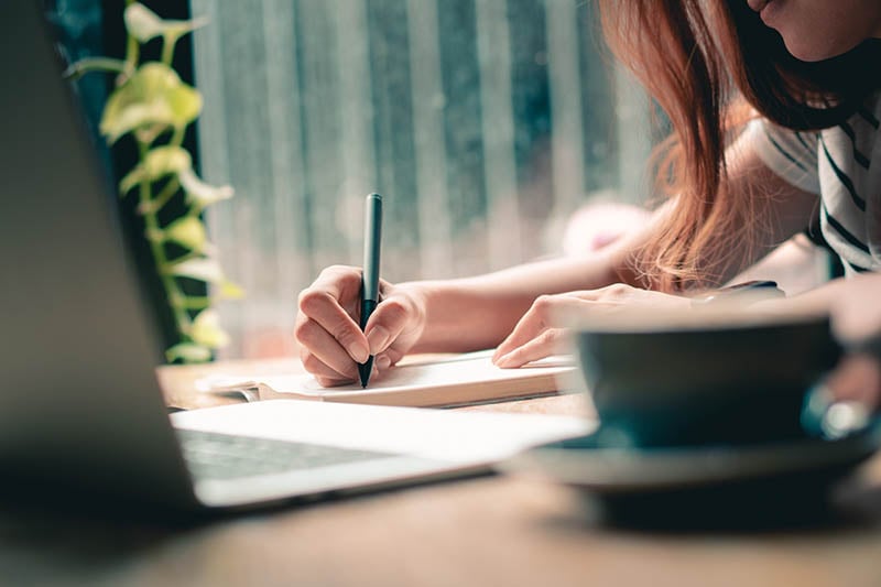 woman writing a shortlist on a notepad with coffee 800